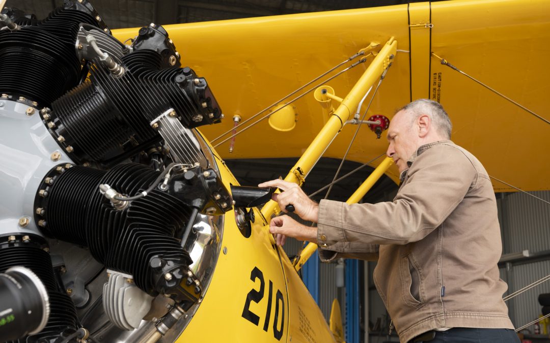 An older man looks over a yellow biplane as he prepares for a flight.